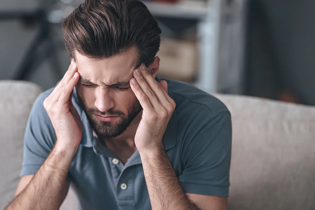 a man sitting down at home and holding his hands to his head in discomfort
