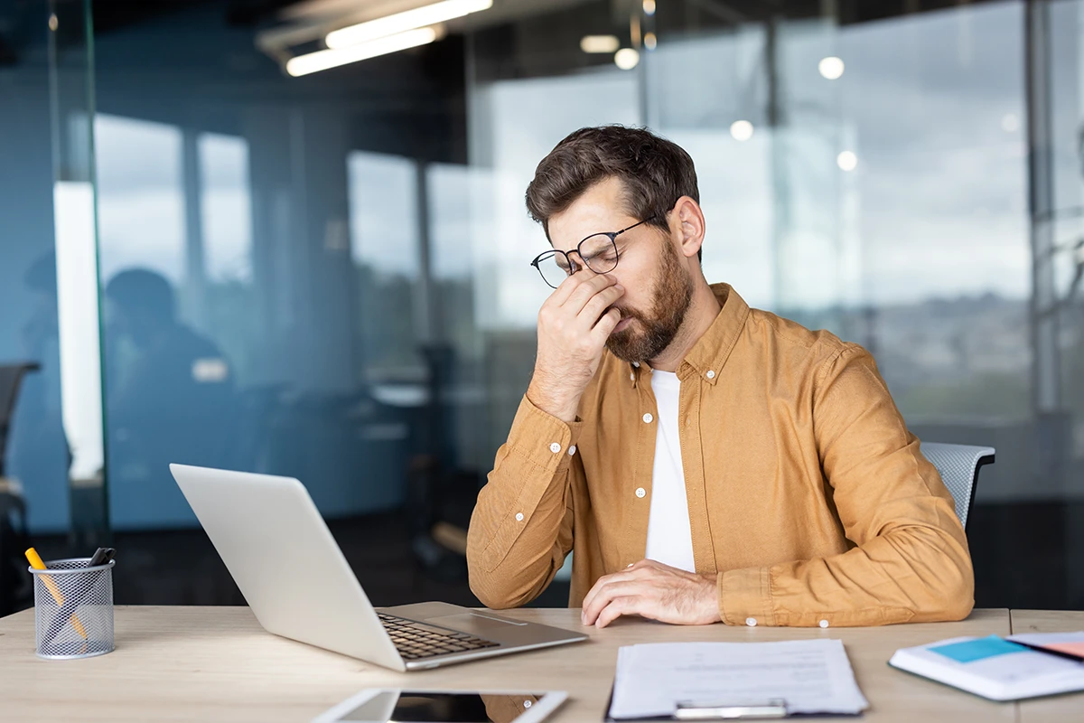 a man sitting at his desk at work and rubbing the bridge of his nose due to discomfort