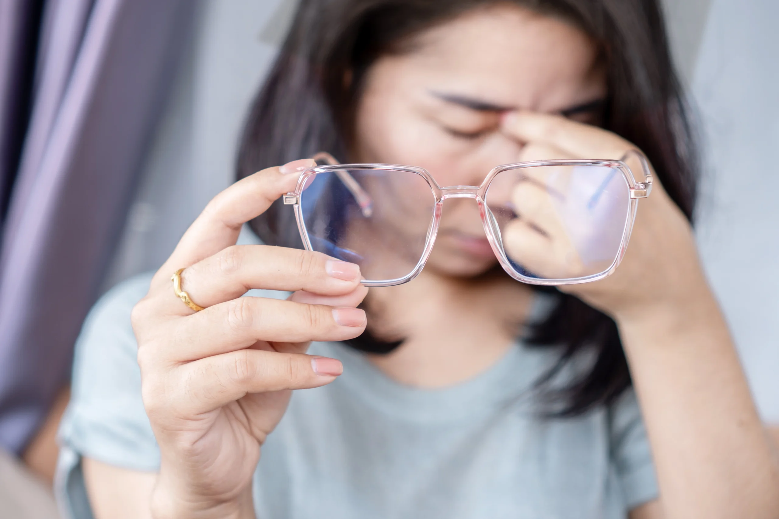 A blurry photo of a woman holding her glasses away from her face, rubbing the bridge of her nose.