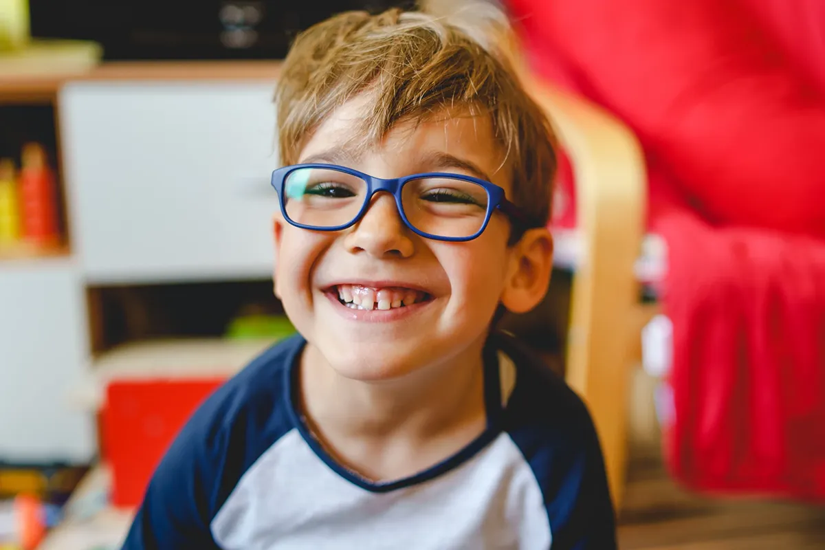 A smiling little boy wearing blue framed glasses.