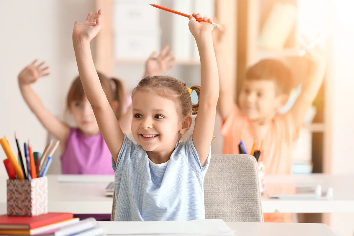 a little girl at school raising her arms along with other kids in the classroom